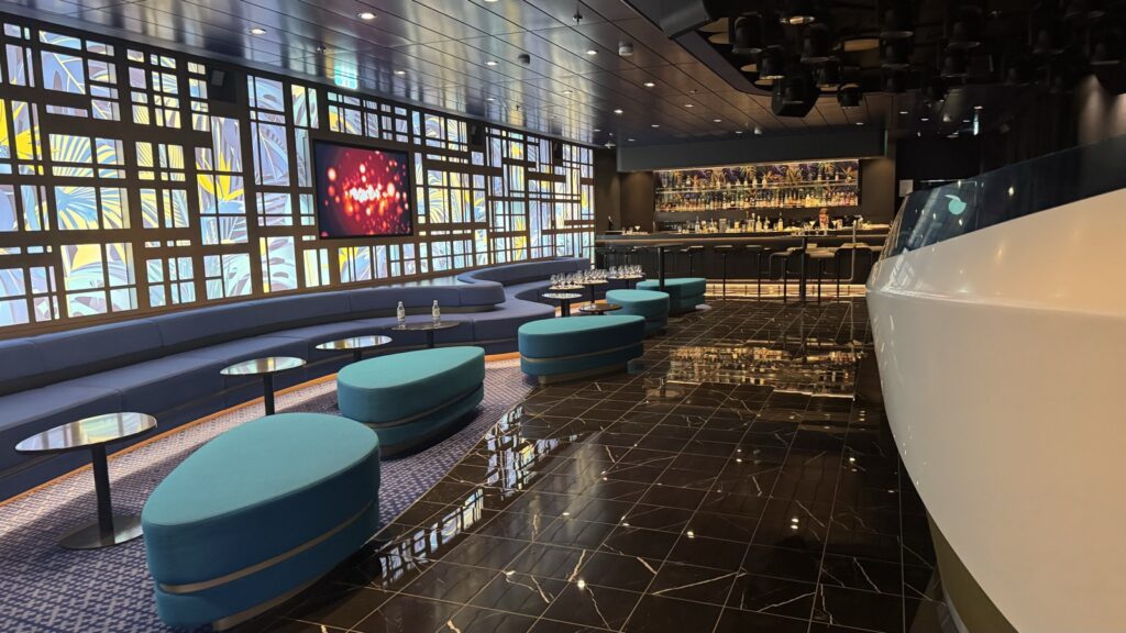 Petrolfarbene Rundbänke und Stehtische in der Abtanz Bar der Mein Schiff 7, rechts der Tresen mit der Flaschenwand