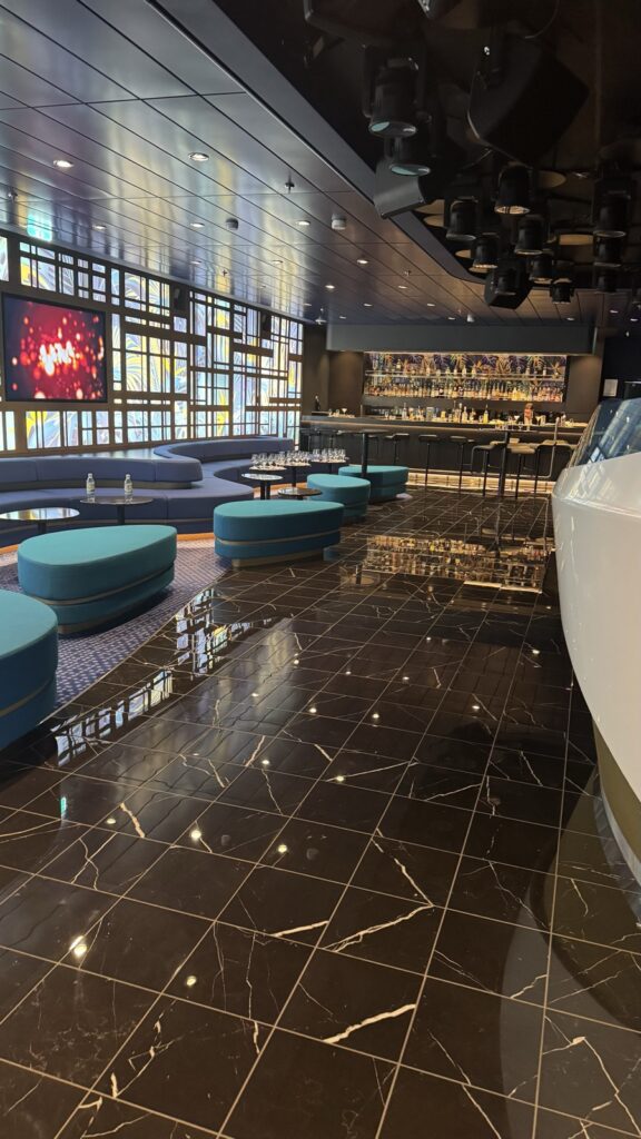 Leere Tanzfläche der Abtanz Bar auf der Mein Schiff 7 mit dunklem Marmorboden, Scheinwerfern an der Decke und der beleuchteten Fensterwand